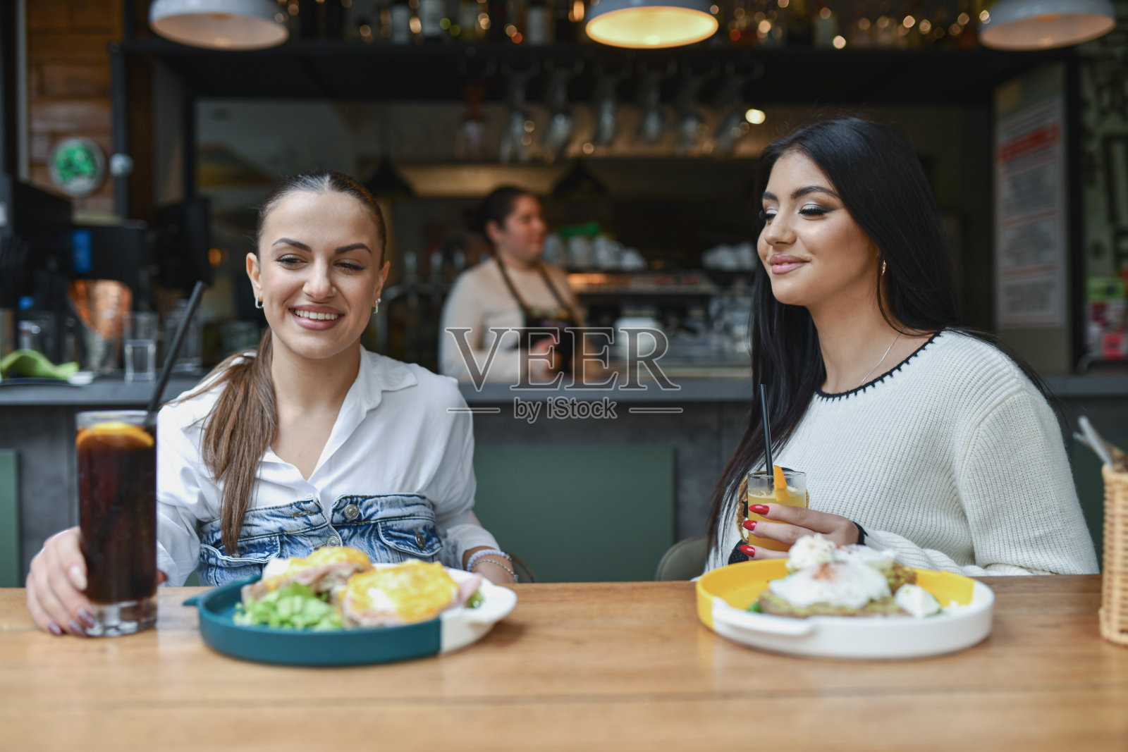 两位女士在酒廊酒吧享用早餐，背景中有饮品和帅气的女服务员。照片摄影图片