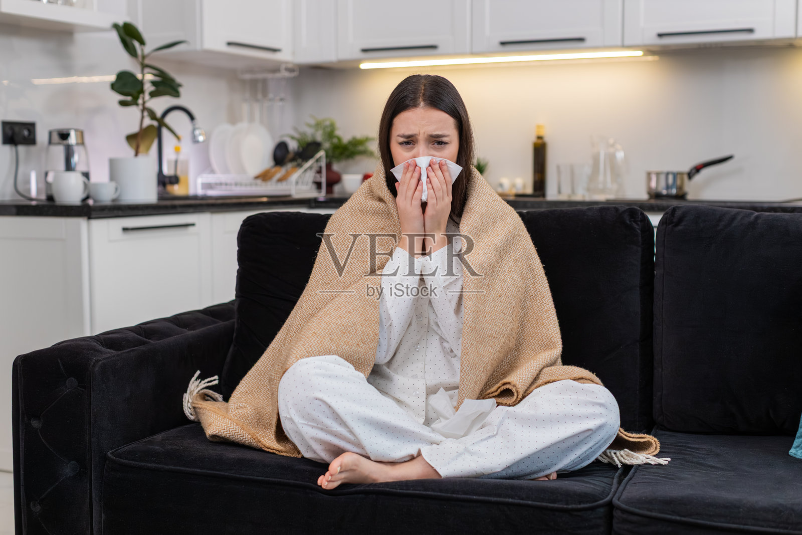 年轻女子裹着毯子打喷嚏，使用纸巾，有感冒、流感症状，流鼻涕，身体不适，生病，疲惫，虚弱照片摄影图片