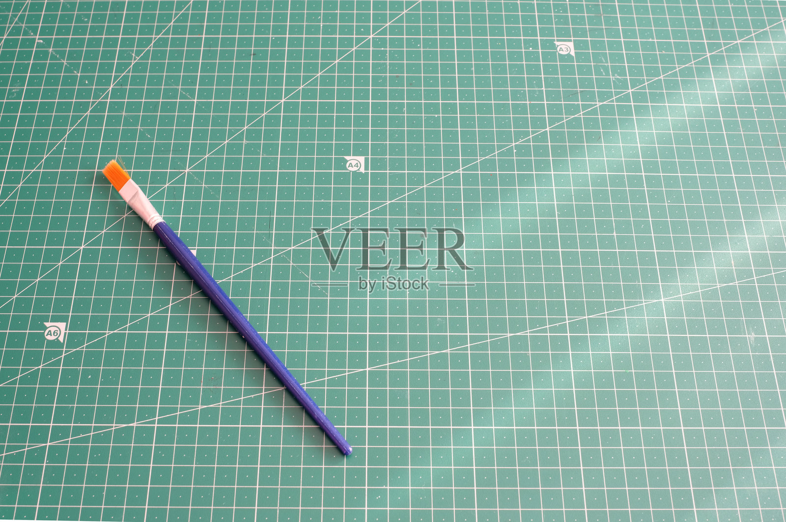 一张蓝橙色画笔斜放在绿色切割垫上，切割垫上印有精确的网格图案，提供了充足的复制空间，这是一个关于艺术设计或教育的简洁概念。照片摄影图片