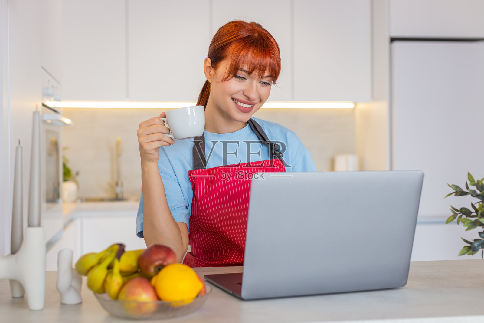 年轻女子在厨房里用笔记本电脑回复邮件，边喝咖啡边专注工作照片摄影图片