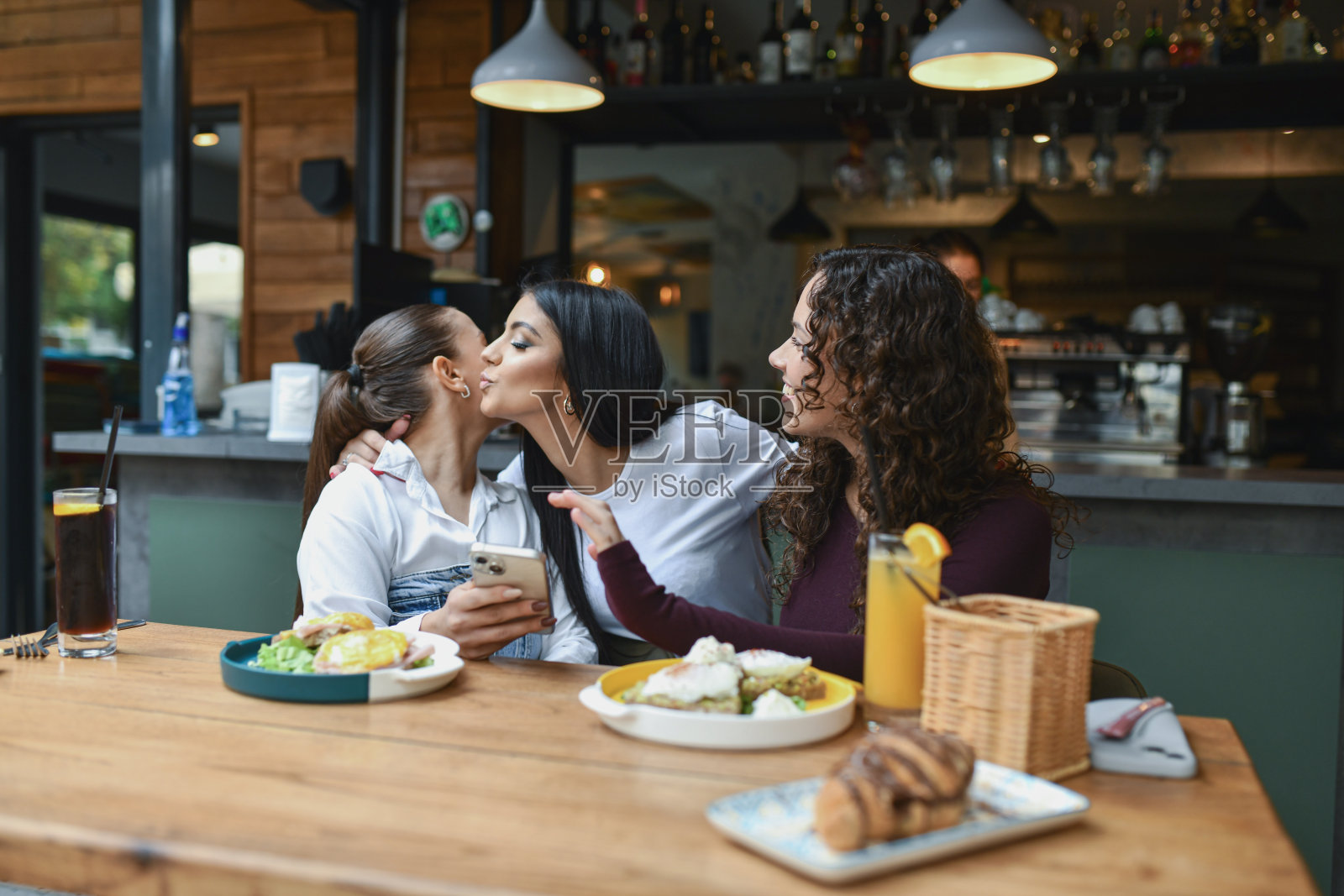 朋友们在舒适的酒吧休息室分享早餐，其中一人亲吻了脸颊，温馨的友谊时刻照片摄影图片