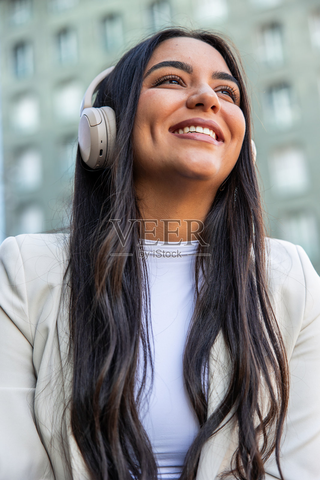 快乐的年轻拉美裔女商人竖屏在城市里听音乐照片摄影图片
