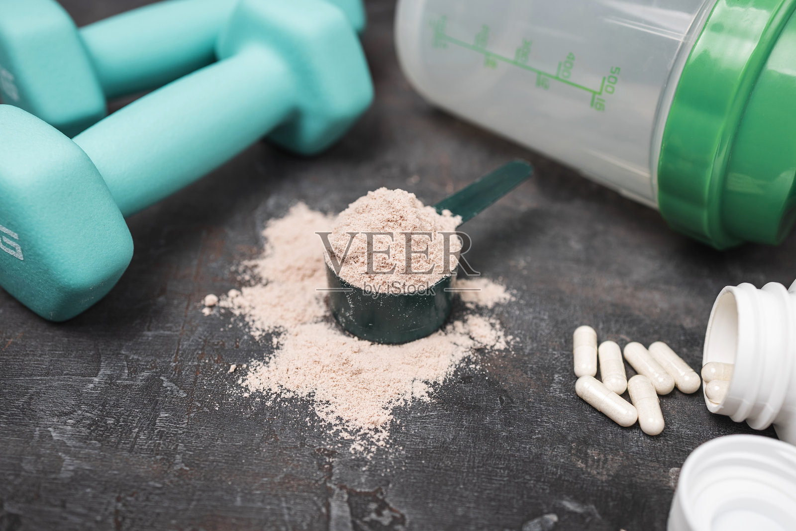 深色背景上的乳清蛋白粉勺、白色氨基酸胶囊、健身哑铃和摇摇杯，运动营养与健康生活方式概念照片摄影图片