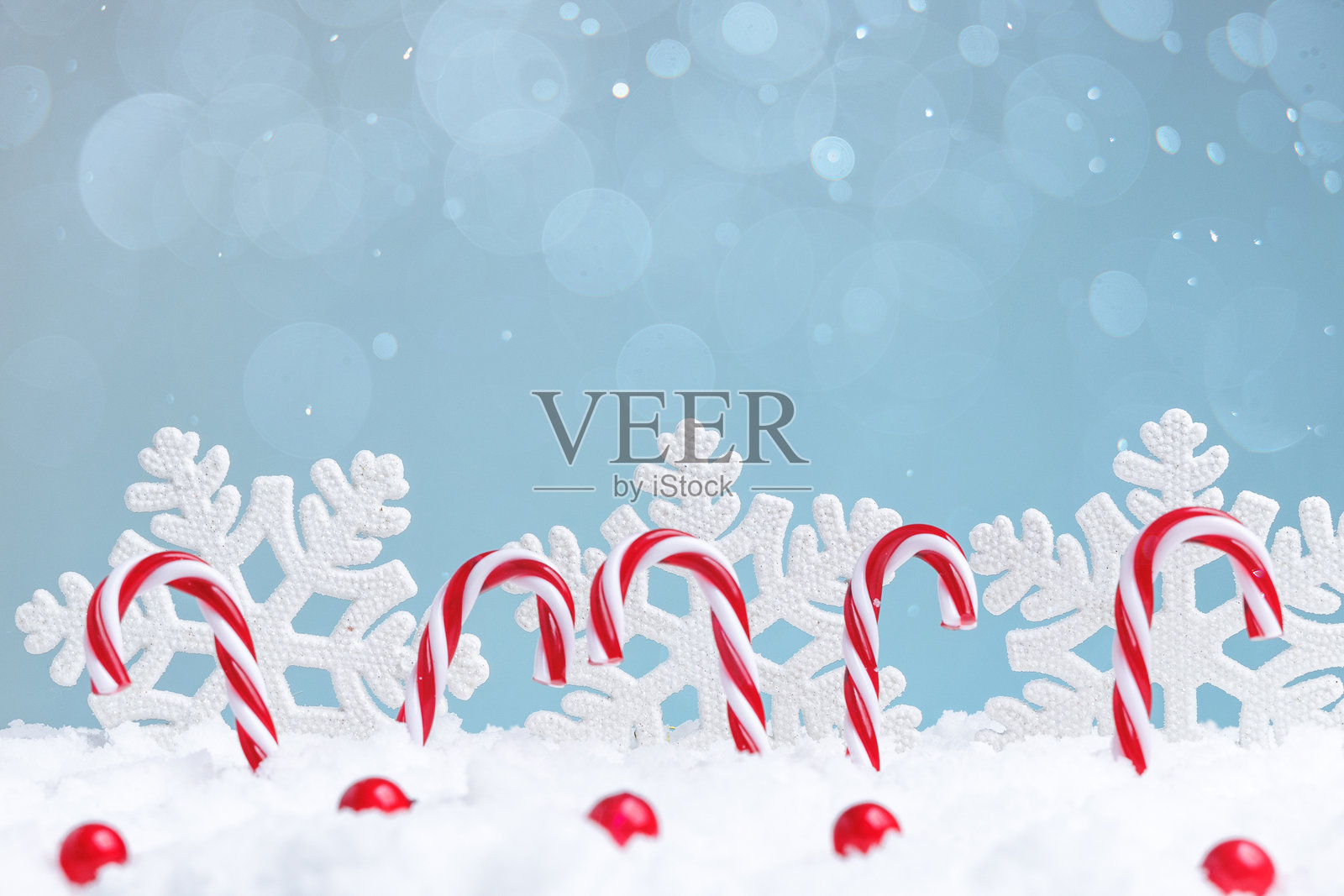 节日里，薄荷糖条纹的糖果摆放在雪白的背景上，点缀着纸雪花，充满欢乐气氛。照片摄影图片