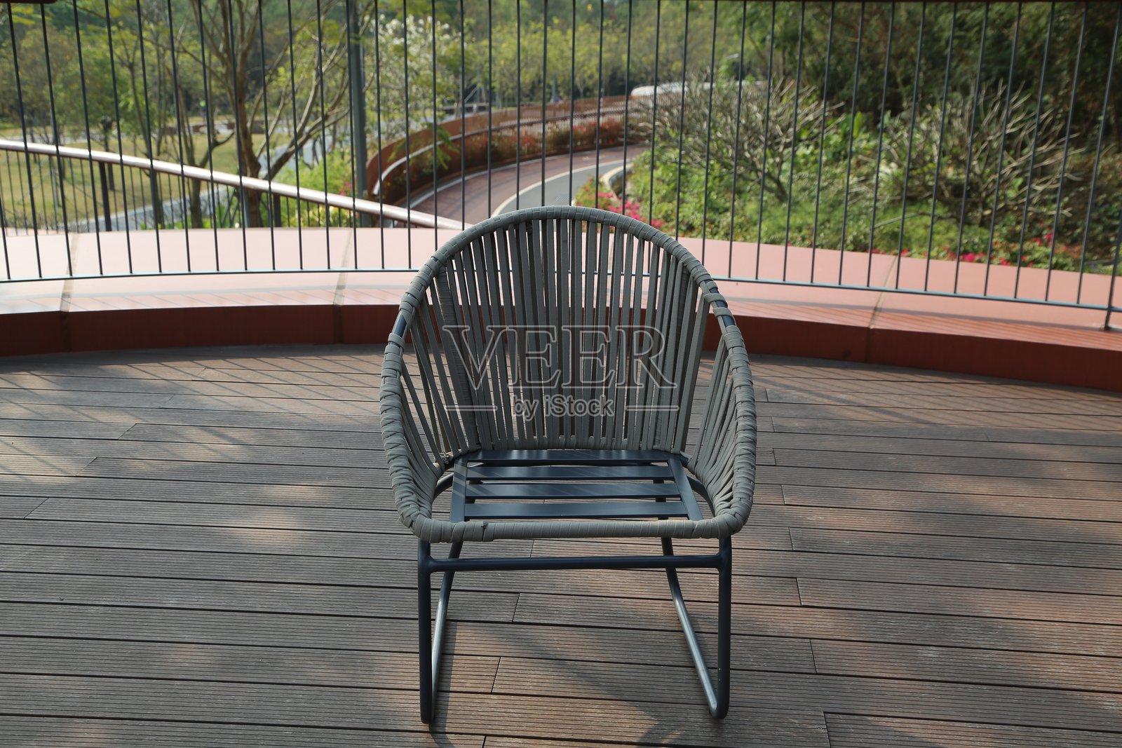 光滑的编织藤椅，灰色钢架和深木纹板条座椅，置于带有木地板的户外公园阳台上照片摄影图片