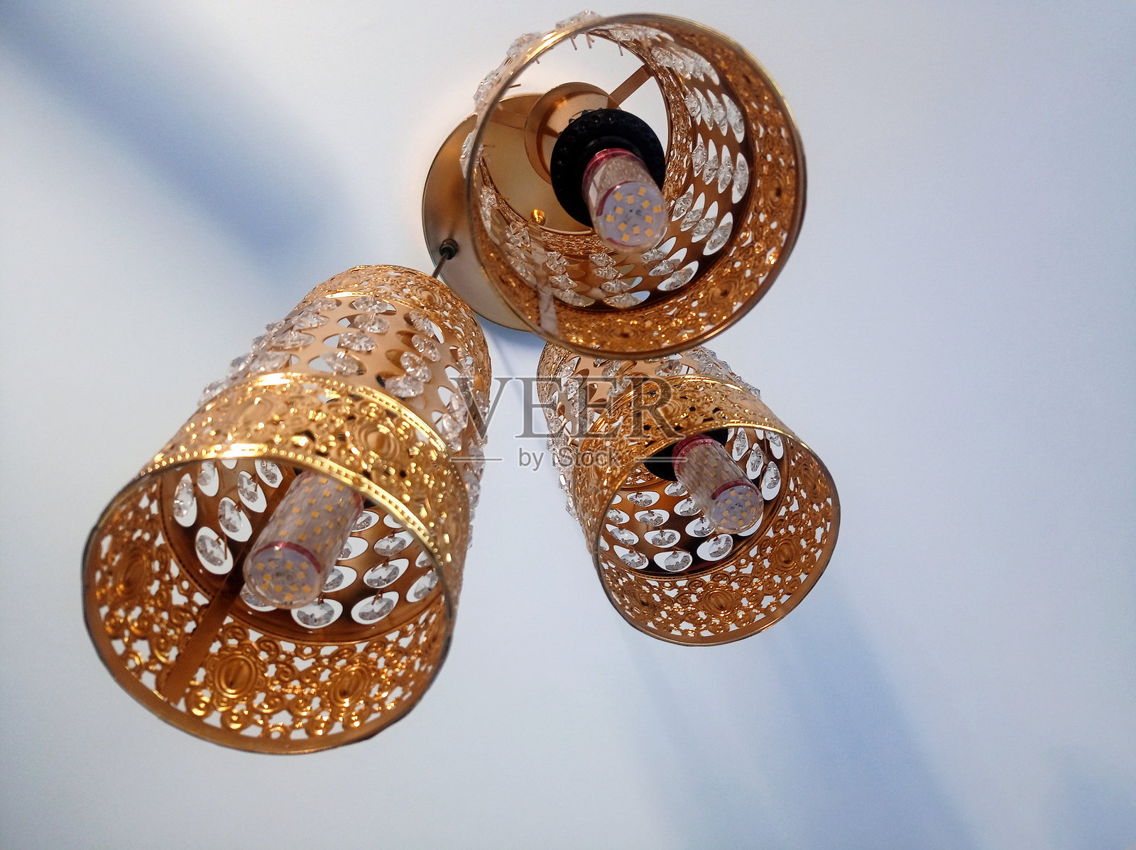 特写镜头，一个装饰性的金色吊灯，带有三个钟形灯，上面装饰着水晶状的元素照片摄影图片