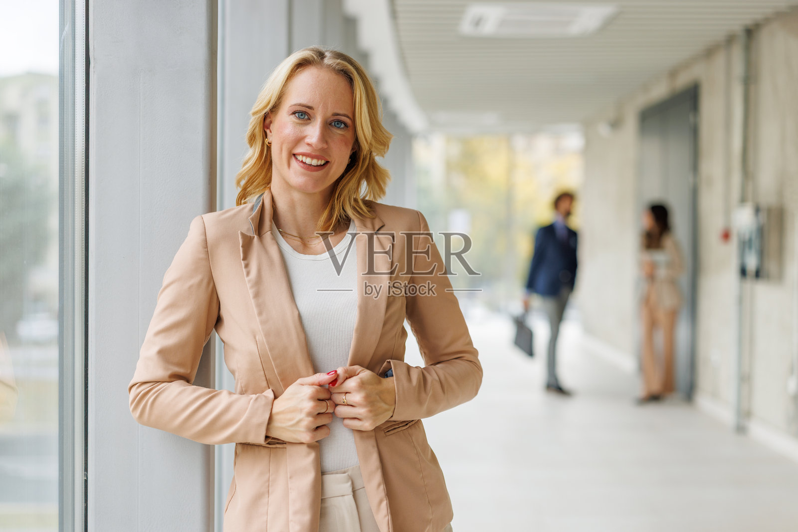 一位自信的商界女性站在现代办公室的走廊里，脸上带着微笑。照片摄影图片