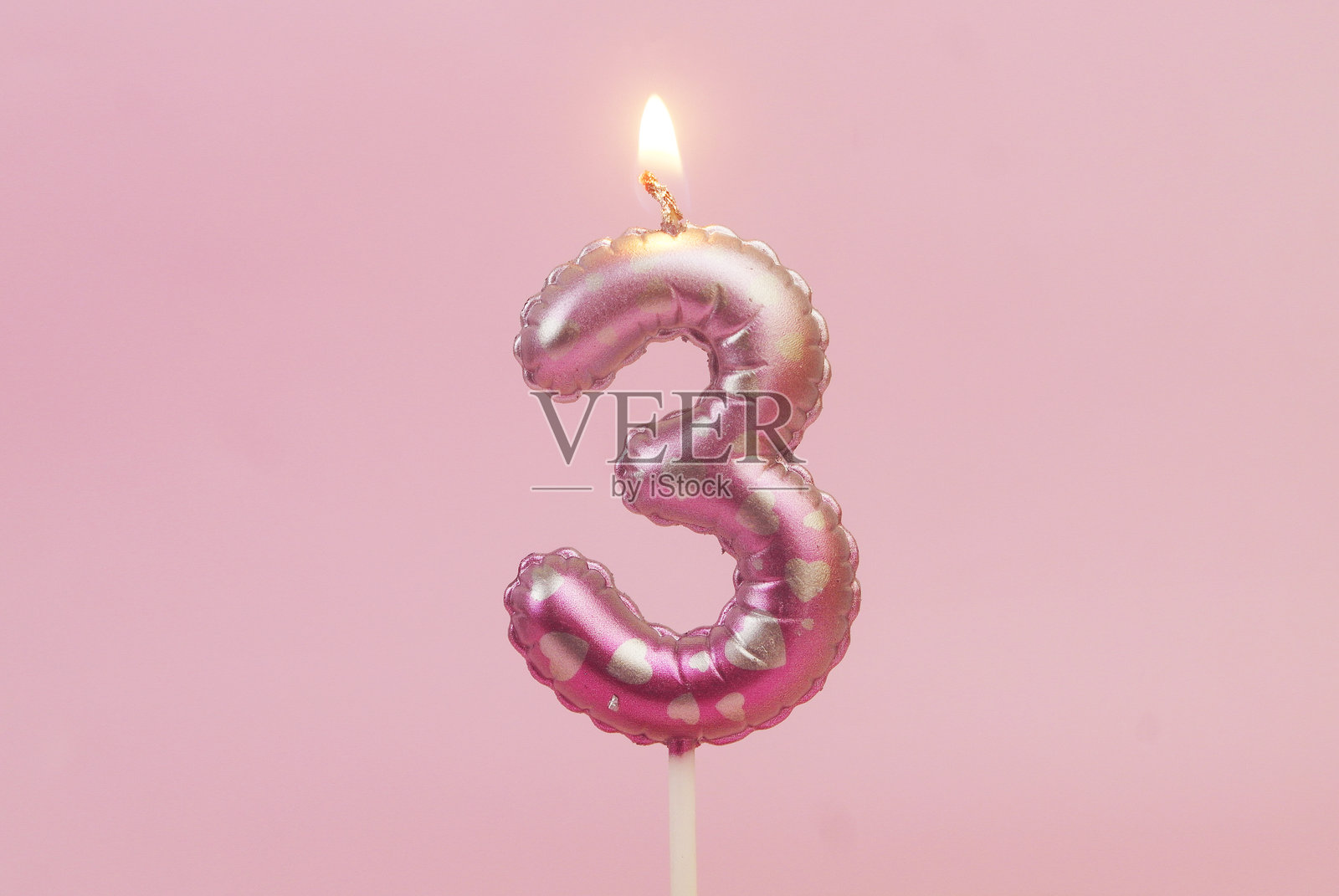 粉色背景上燃烧的粉色生日蜡烛，上面有心形图案，数字为3照片摄影图片