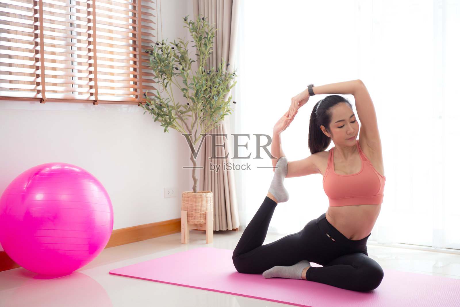 年轻亚洲女性在家客厅的瑜伽垫上练习瑜伽，伸展背部肌肉，她充满挑战和动力地进行普拉提锻炼，以实现健康、运动和身心健康。照片摄影图片
