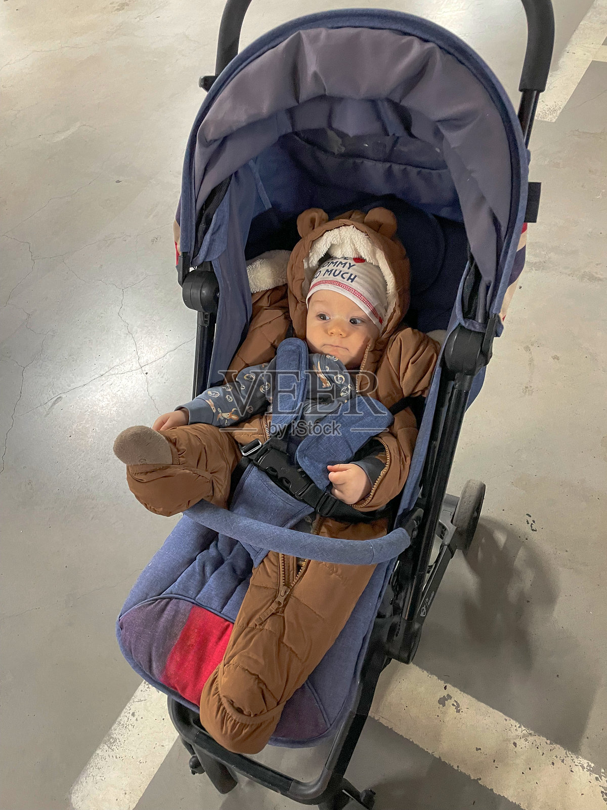 穿着棕熊风格雪服的婴儿舒适地躺在停车区的婴儿车里照片摄影图片