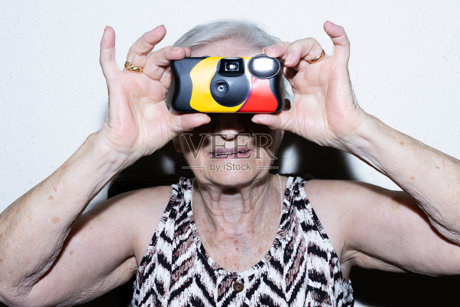 一位年长的女士，手持一次性胶片相机，面带微笑照片摄影图片