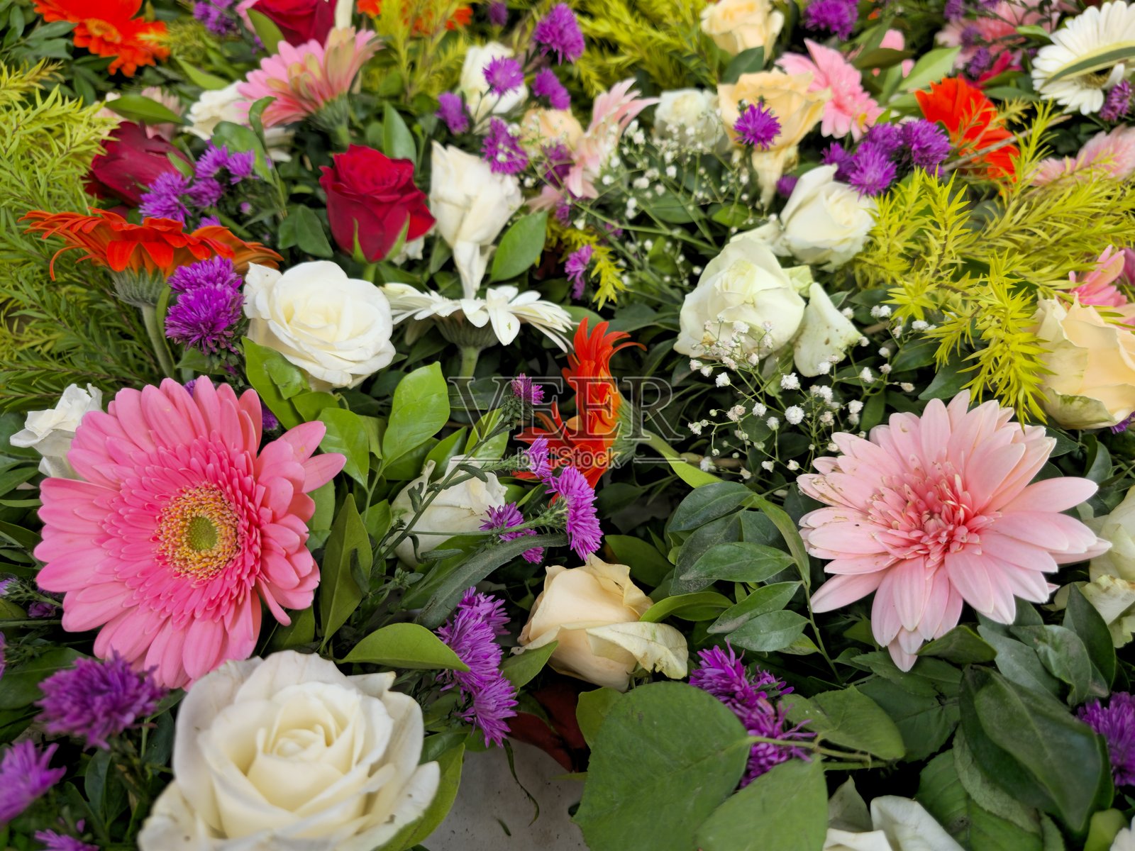 色彩鲜艳的混合鲜花插花，包括玫瑰、非洲菊和绿叶，展示出充满活力的图案照片摄影图片