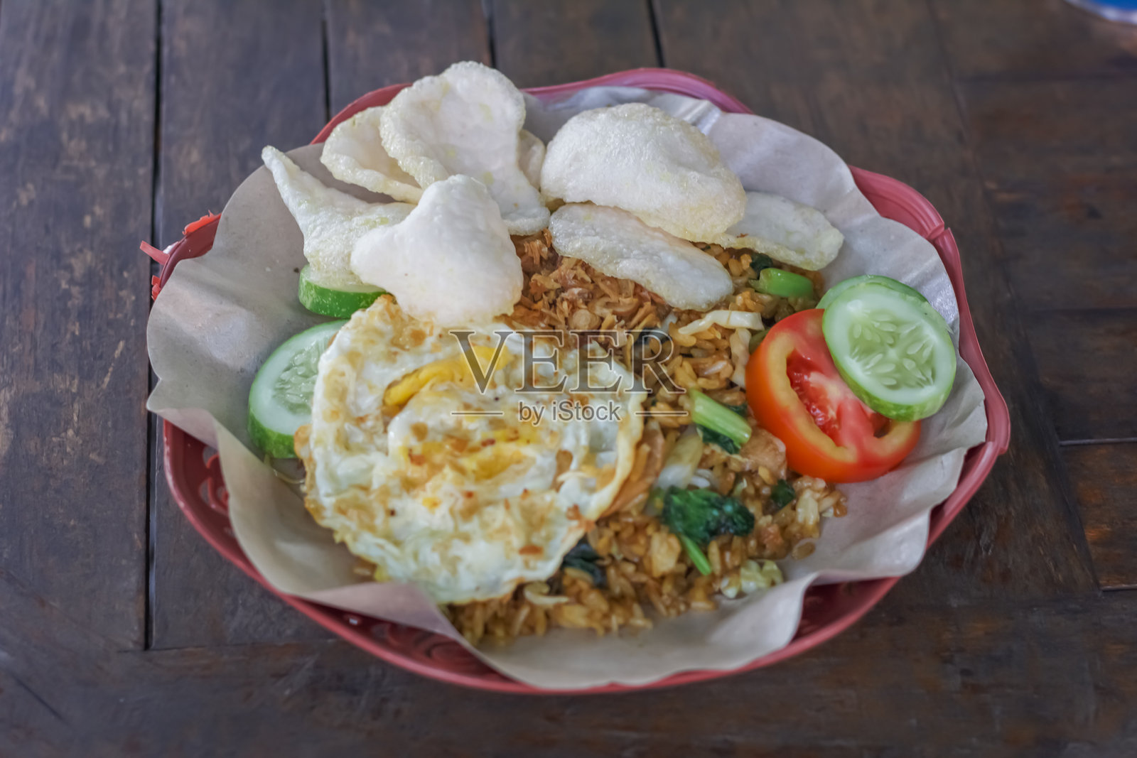 印尼炒饭（nasi goreng），配以煎蛋、脆饼、黄瓜和番茄，摆放在木桌上。照片摄影图片