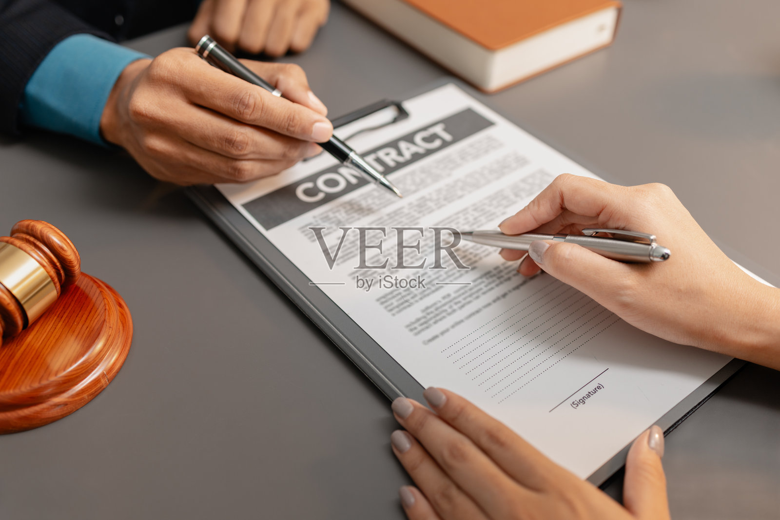 一位身穿西装的男律师与一位女客户讨论合同细节，并指向法律文件上的签名处。办公桌上摆放着象征法律与正义的法槌。照片摄影图片