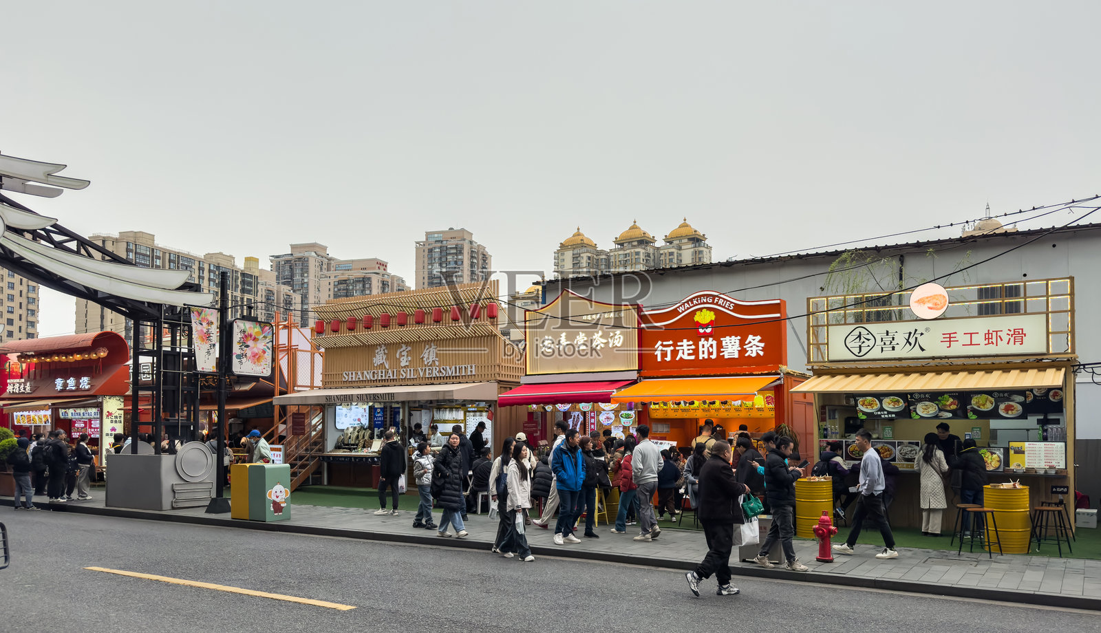 中国上海。熙熙攘攘的人群在热闹的街头食品市场里漫步，背景是色彩斑斓的摊位和现代建筑照片摄影图片