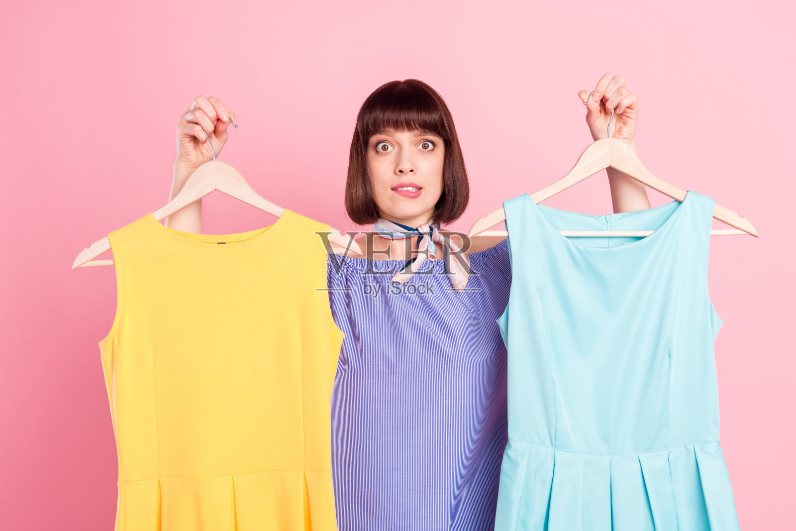 一名女子在购物时试穿衣服，她显得犹豫不决，不确定地咬着嘴唇，背景是柔和的粉色。照片摄影图片