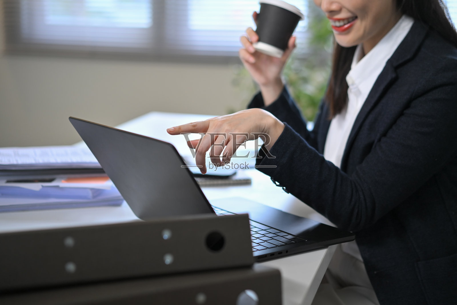 特写一位女商人在使用笔记本电脑并喝咖啡时微笑的镜头，代表着职业生活方式。照片摄影图片