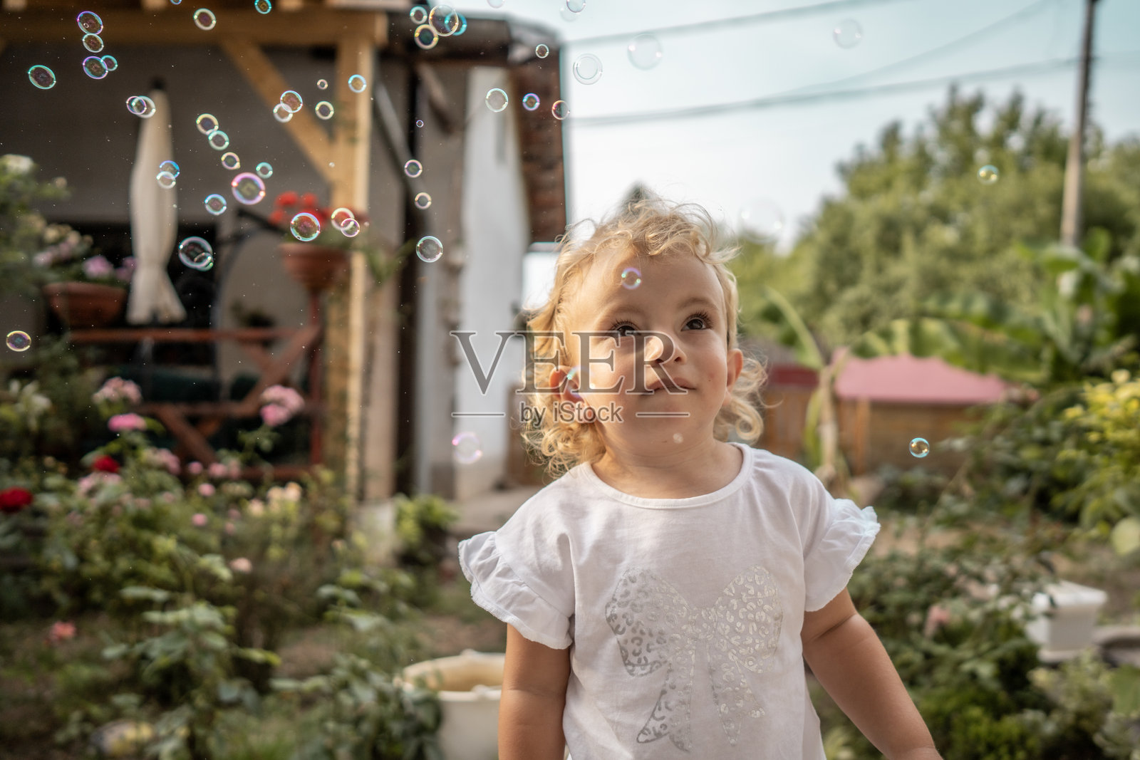 充满阳光的花园里，一个好奇的小女孩仰望着漂浮的泡泡照片摄影图片