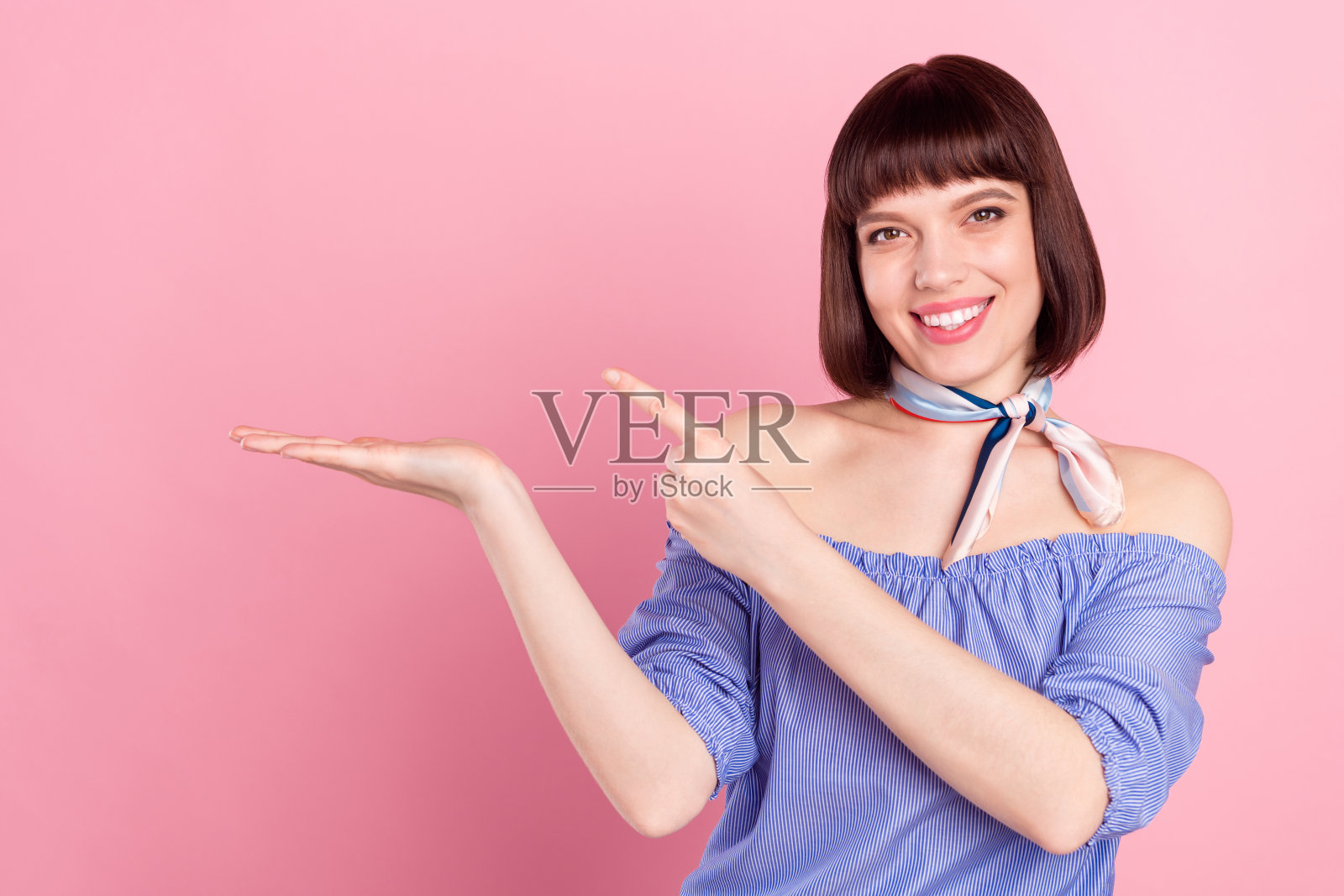 快乐的年轻女子伸出手指，手握着空白空间，孤立在粉色背景上照片摄影图片