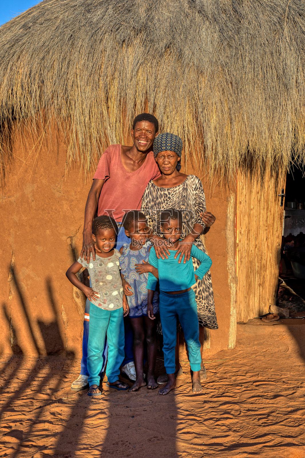 非洲村庄里，一家人（父母和女儿）面带笑容，站在茅草屋的门前照片摄影图片