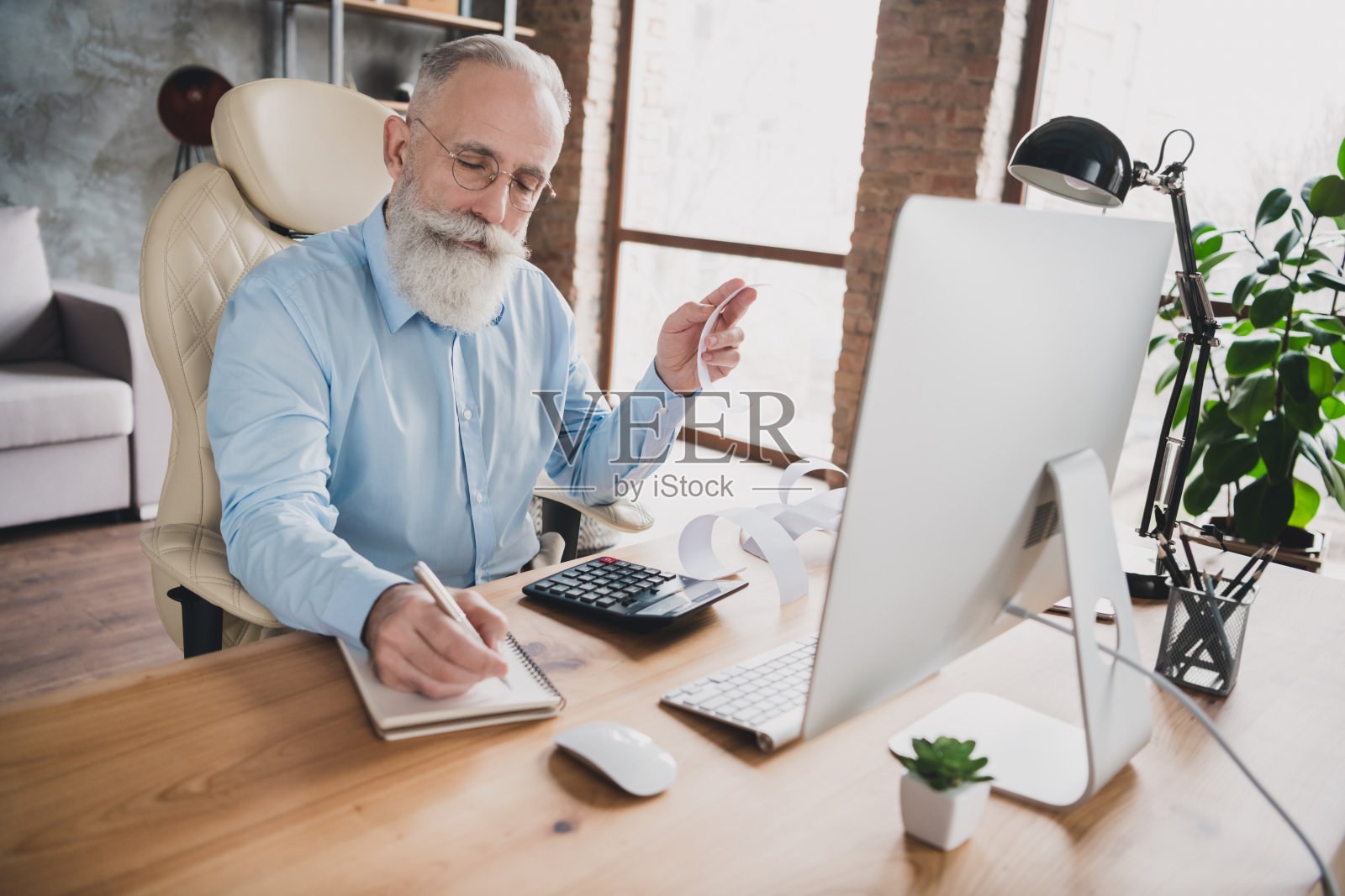 照片：严肃专注的老年退休会计在办公室工作站内写笔记照片摄影图片