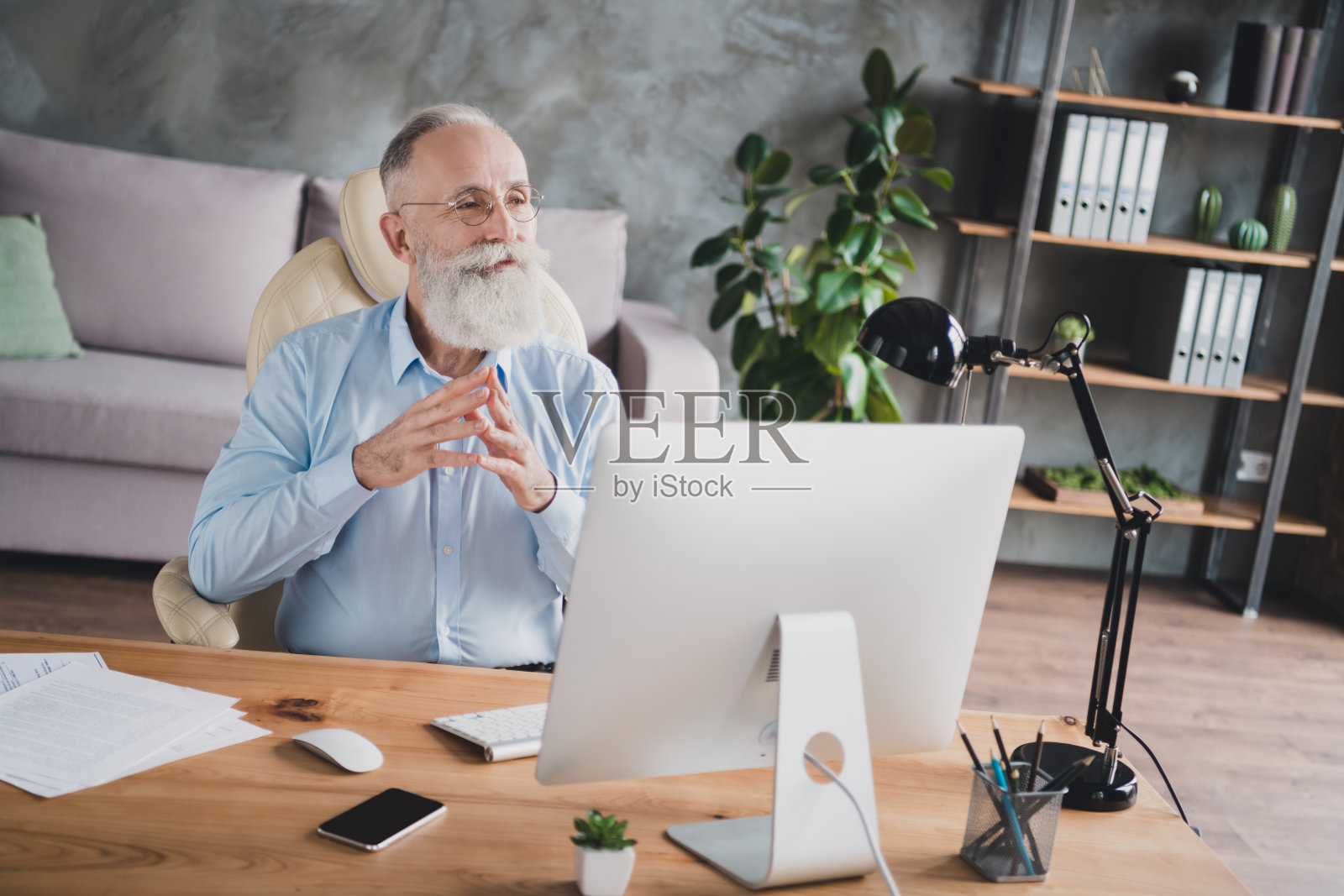 照片：一位有吸引力的、深思熟虑的、留着胡子的、年龄适中的男士穿着蓝色衬衫，双手手指相碰，在室内工作坊、工作站或工作场所。照片摄影图片