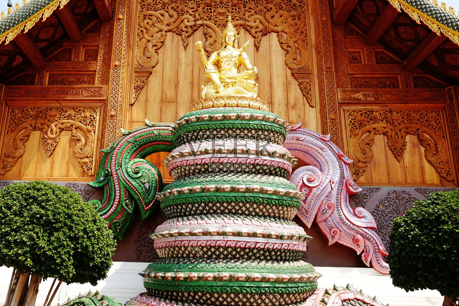 泰国寺庙内，金色的佛像庄严地坐于那迦（蛇神）雕像之上，背景为精美的木雕。照片摄影图片