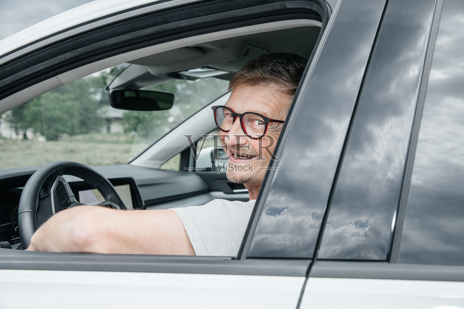 一位成熟的高加索男性在车内驾驶座上微笑着，背景为户外。照片摄影图片