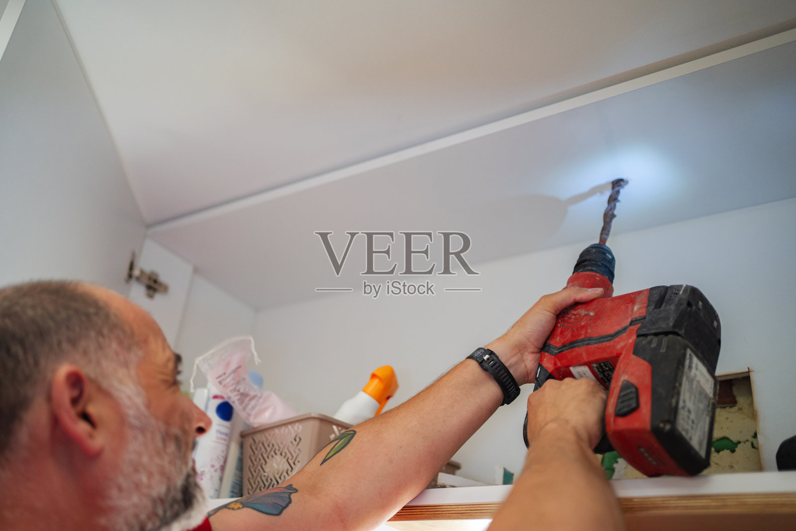 装修工用无绳锤钻在浴室柜的天花板上钻孔照片摄影图片