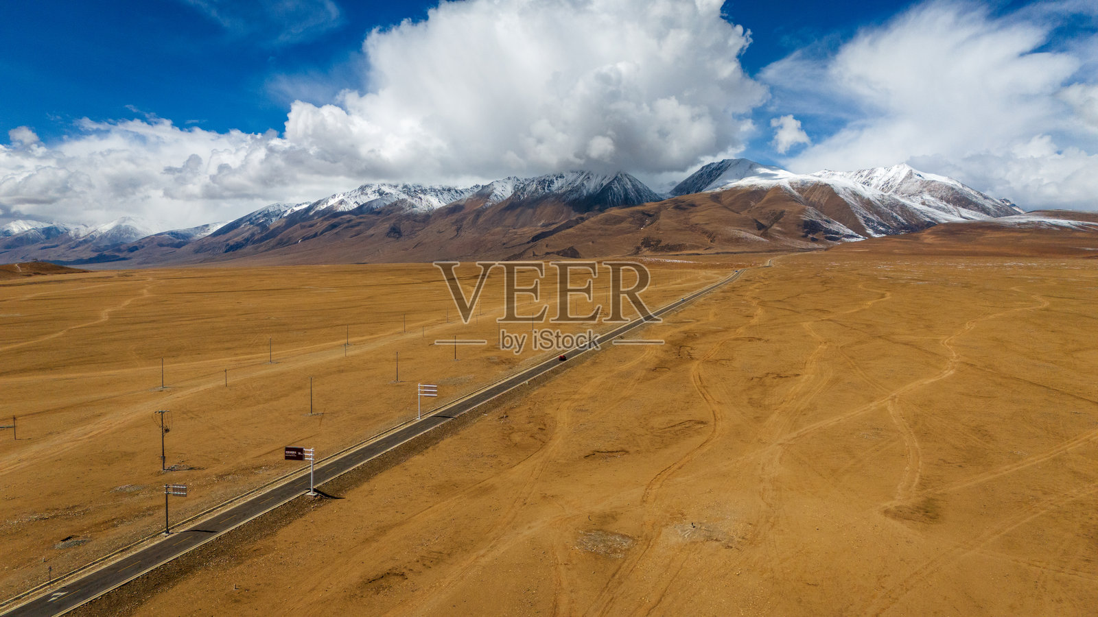 一条无尽的公路穿越荒凉的高原，在戏剧性的云彩和白雪皑皑的山峰下延伸，象征着孤独、自由以及穿越广阔偏远景观的旅程。照片摄影图片
