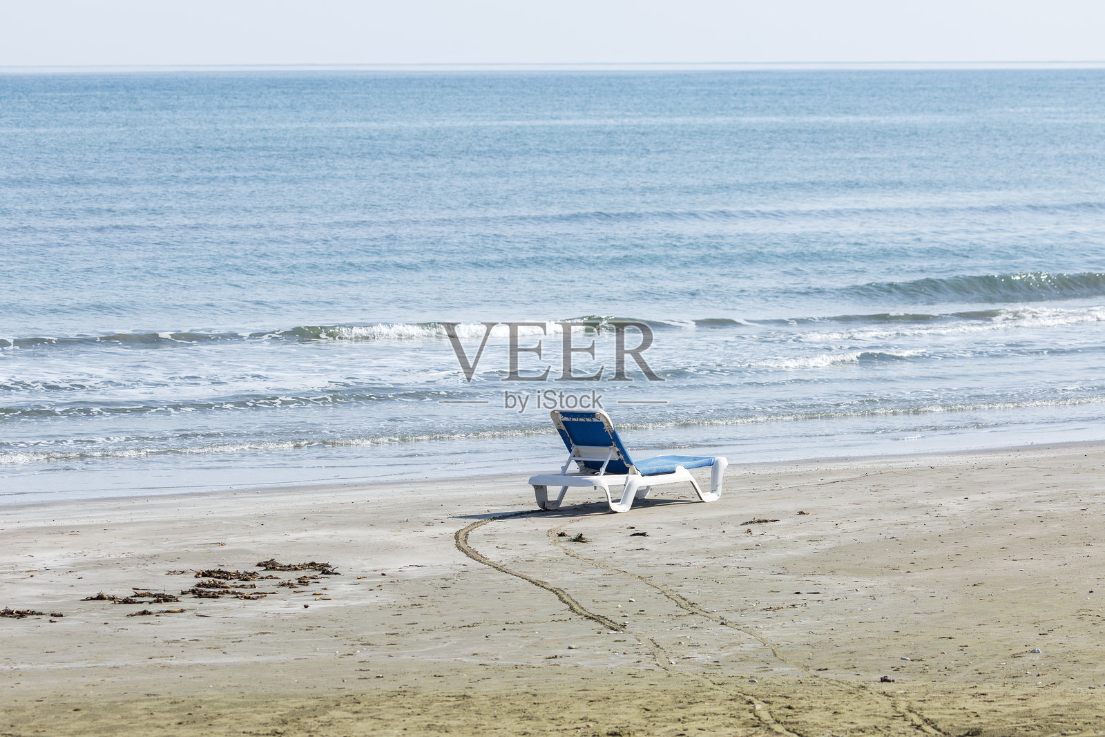一张单独的、空着的蓝白相间的沙滩躺椅，放置在宽阔的沙滩上。这张空椅子象征着一份宁静的邀请，邀请人们前来放松，享受淡季的宁静。照片摄影图片
