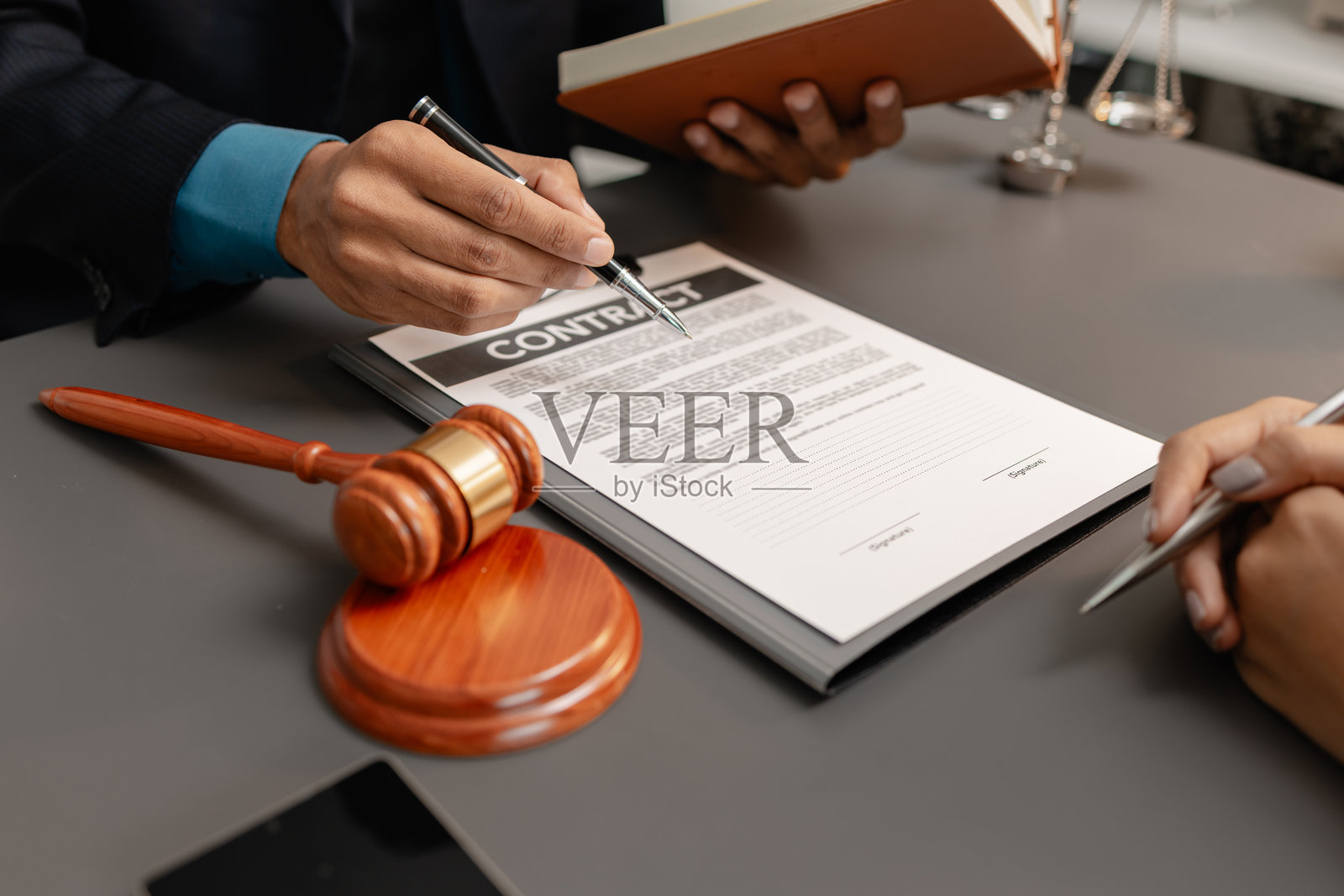 一位身穿西装的男律师正在与一位女客户讨论合同细节，并指向法律文件上的签名区域。办公室的桌子上放着象征法律与正义的法槌。照片摄影图片