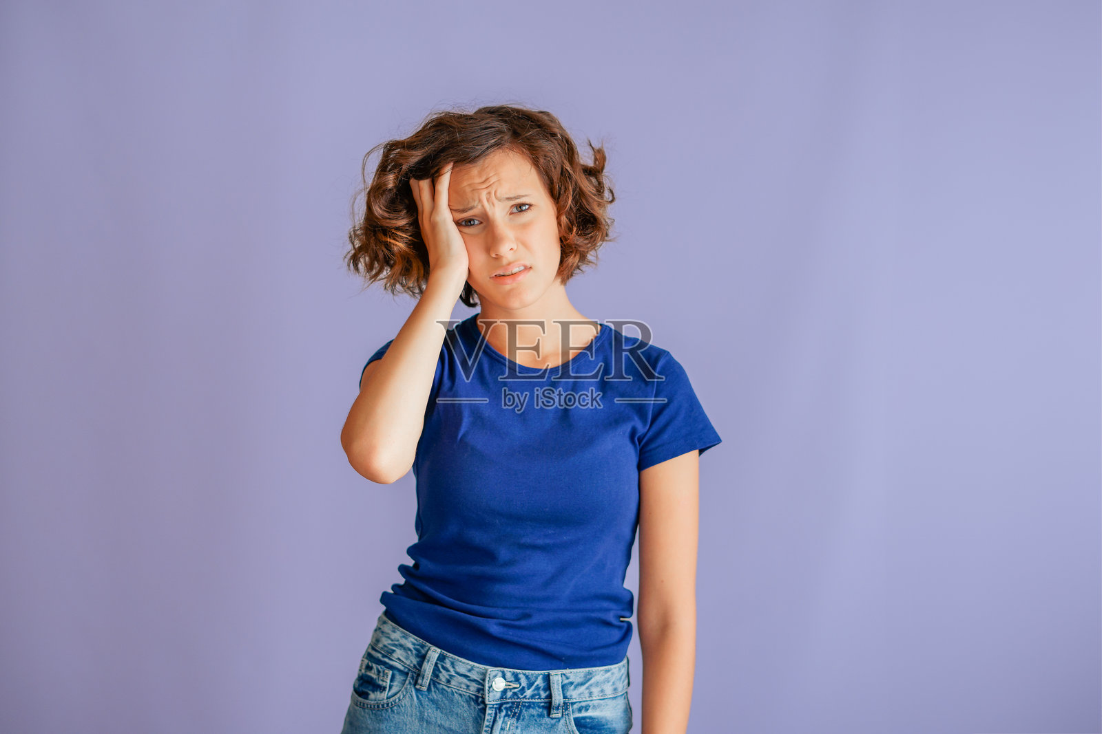 沮丧的年轻女学生，双手抱头，表情悲伤，显示出学习上的失意和失败感，背景为充满活力的蓝色工作室，散发着挫败的能量照片摄影图片