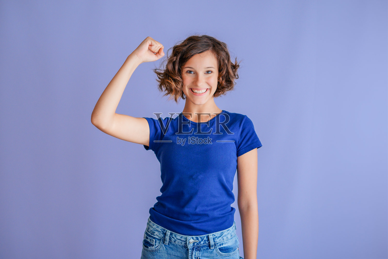 年轻女子成功的庆祝，高举双拳，在充满活力的蓝色工作室背景上展现胜利和喜悦照片摄影图片