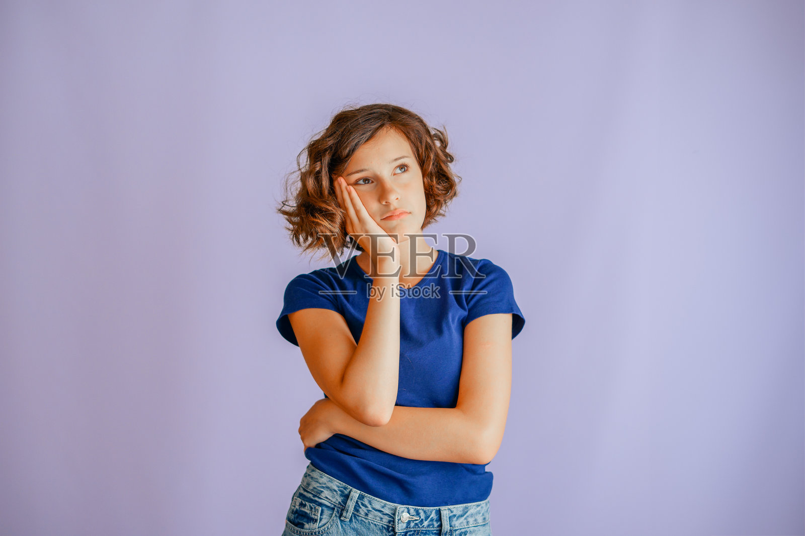 一个年轻女孩若有所思，手托着头，展现出专注的神情和氛围，在充满活力的蓝色工作室背景下，传递出认真的能量，仿佛在做决定。照片摄影图片