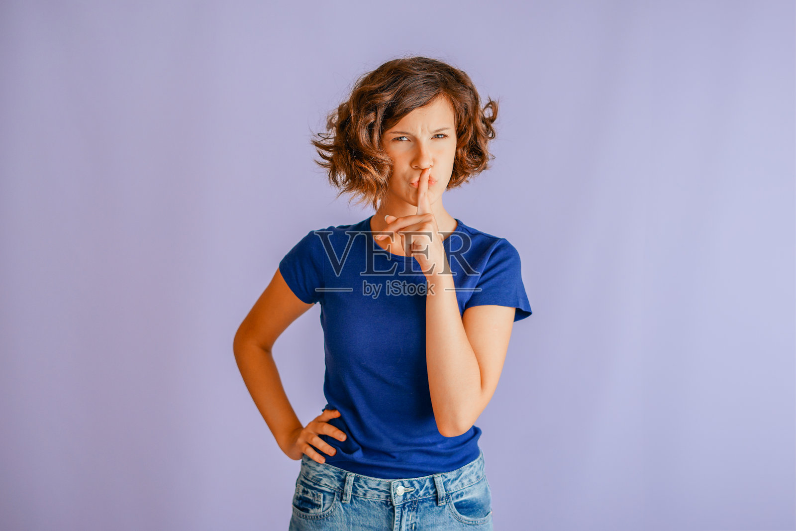 年轻女子专注地用手指放在嘴唇上示意保密，散发出严肃的气场，背景为充满活力的蓝色工作室，充满专注的能量照片摄影图片