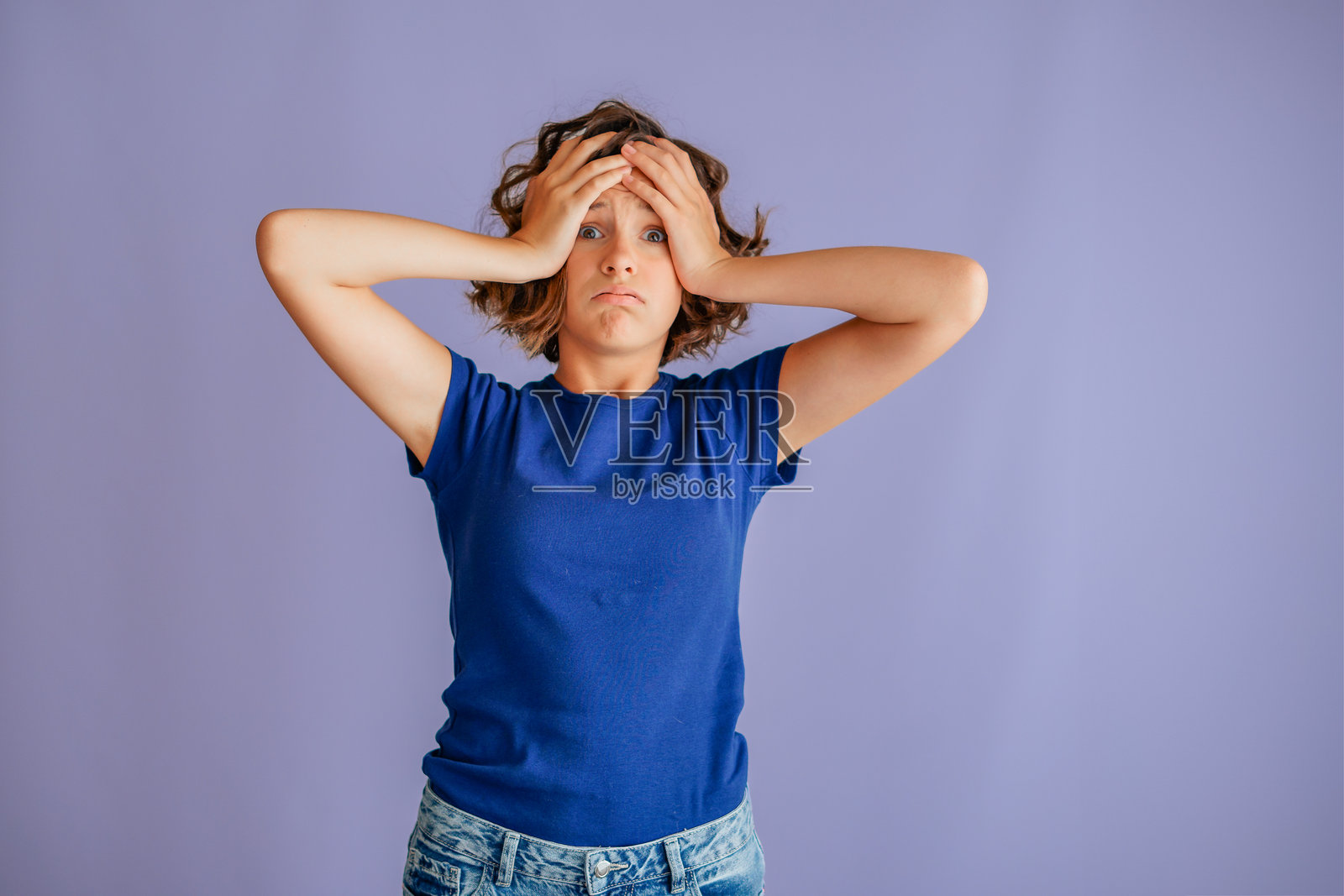 沮丧的年轻女子，双手抱头，愁眉苦脸，充满失败计划的悲伤氛围，背景为充满沮丧能量的鲜艳蓝色影棚。照片摄影图片