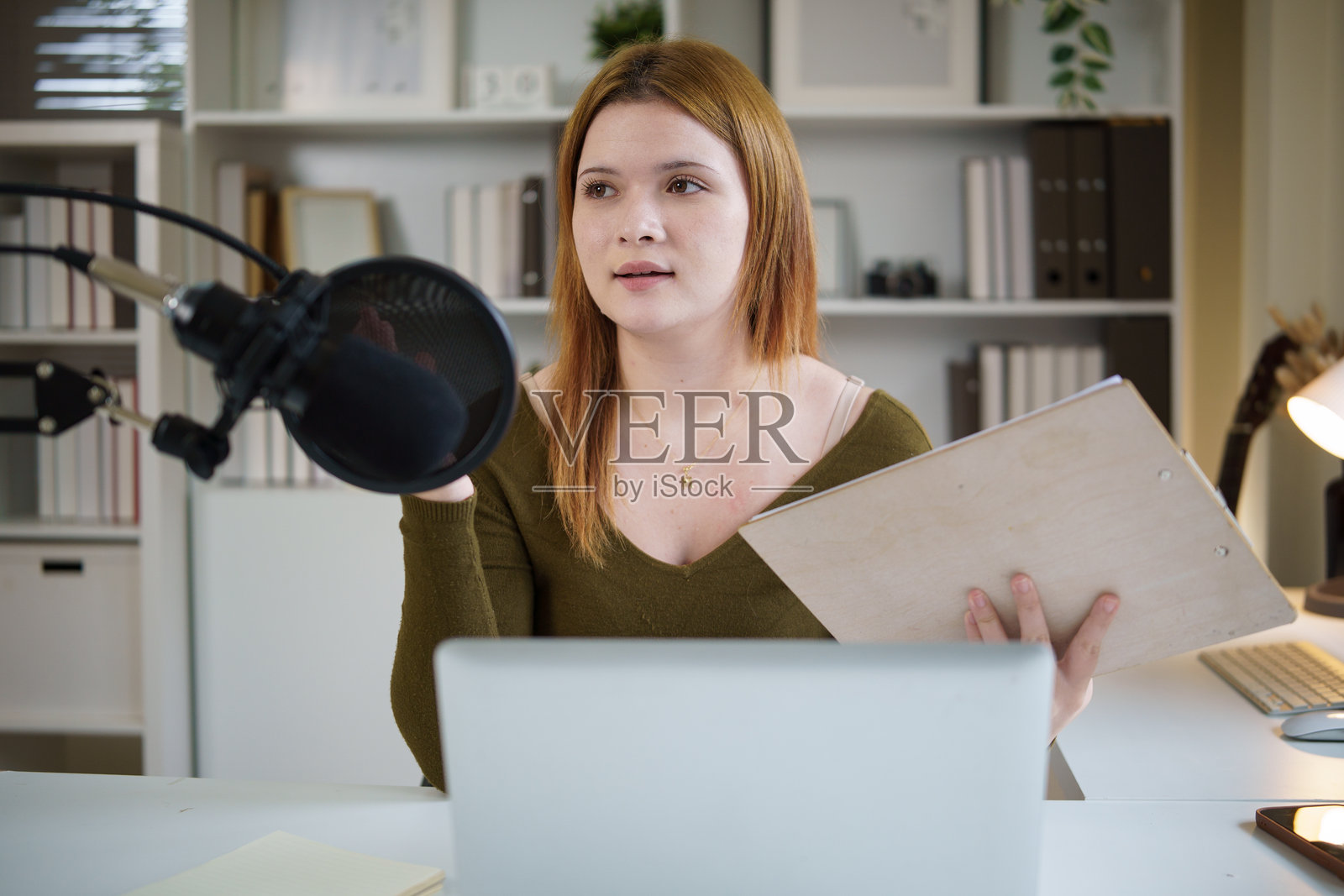快乐的年轻女子正在她的书桌前录制播客。照片摄影图片
