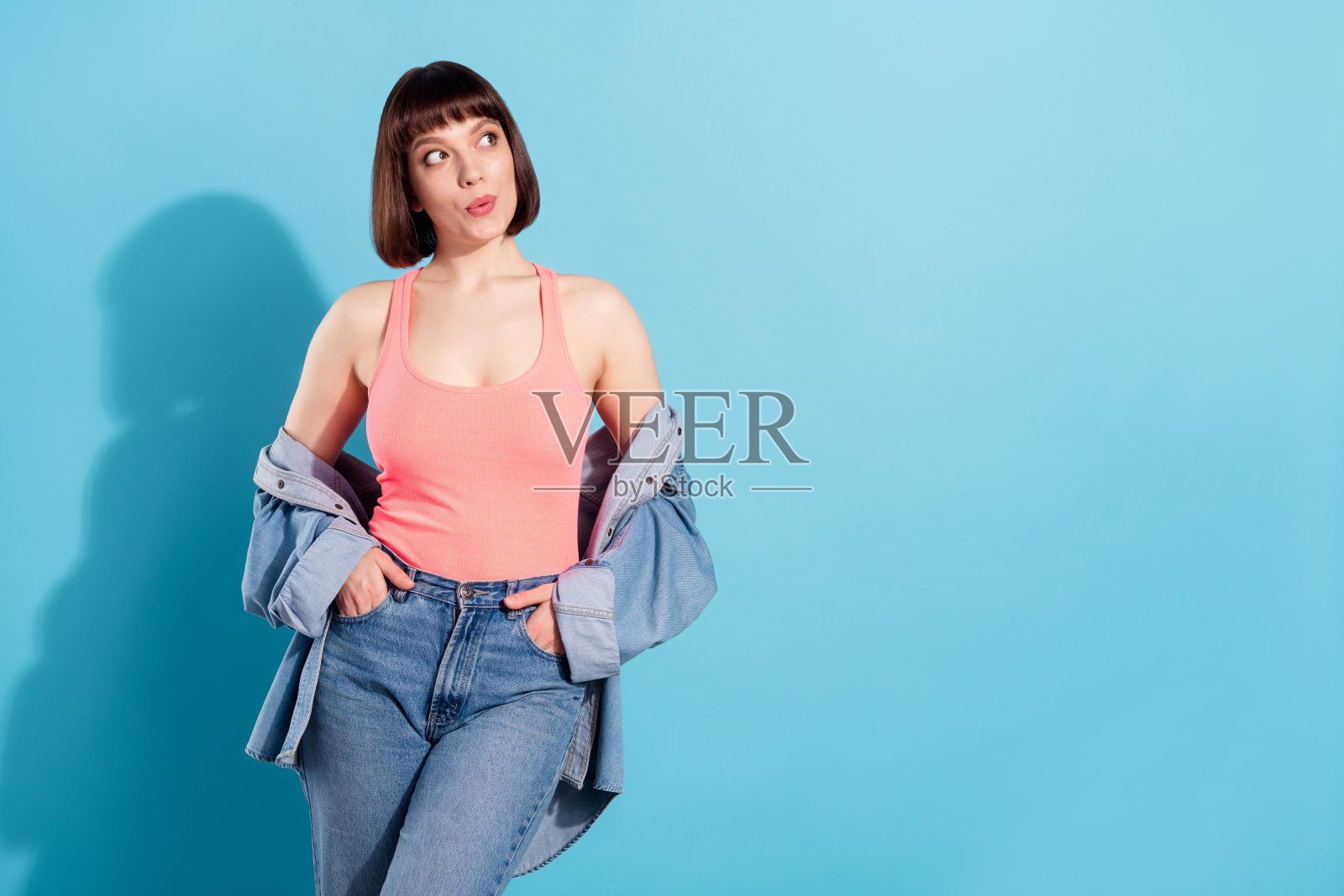 身穿牛仔衬衫的可爱梦幻年轻女子，孤立在蓝色背景下，眼神空洞地望着远方照片摄影图片