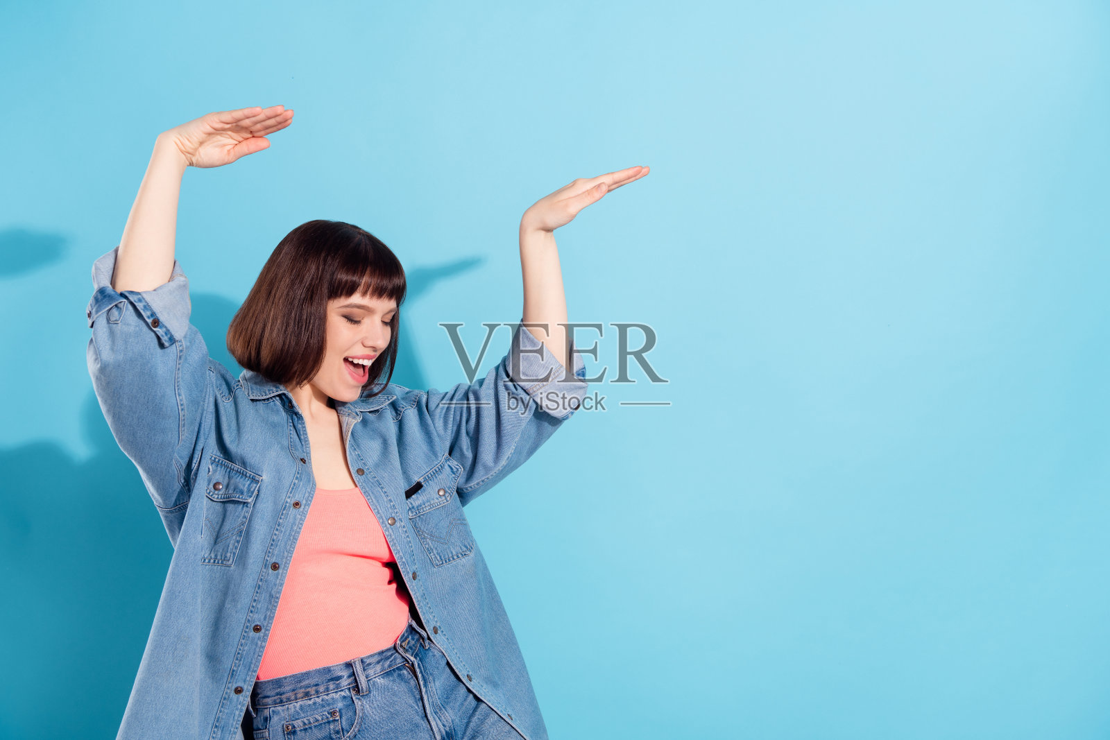 一位迷人的、快乐的、酷炫的女孩的肖像，她在明亮的蓝色背景上跳舞、玩乐，并留有空白空间。照片摄影图片