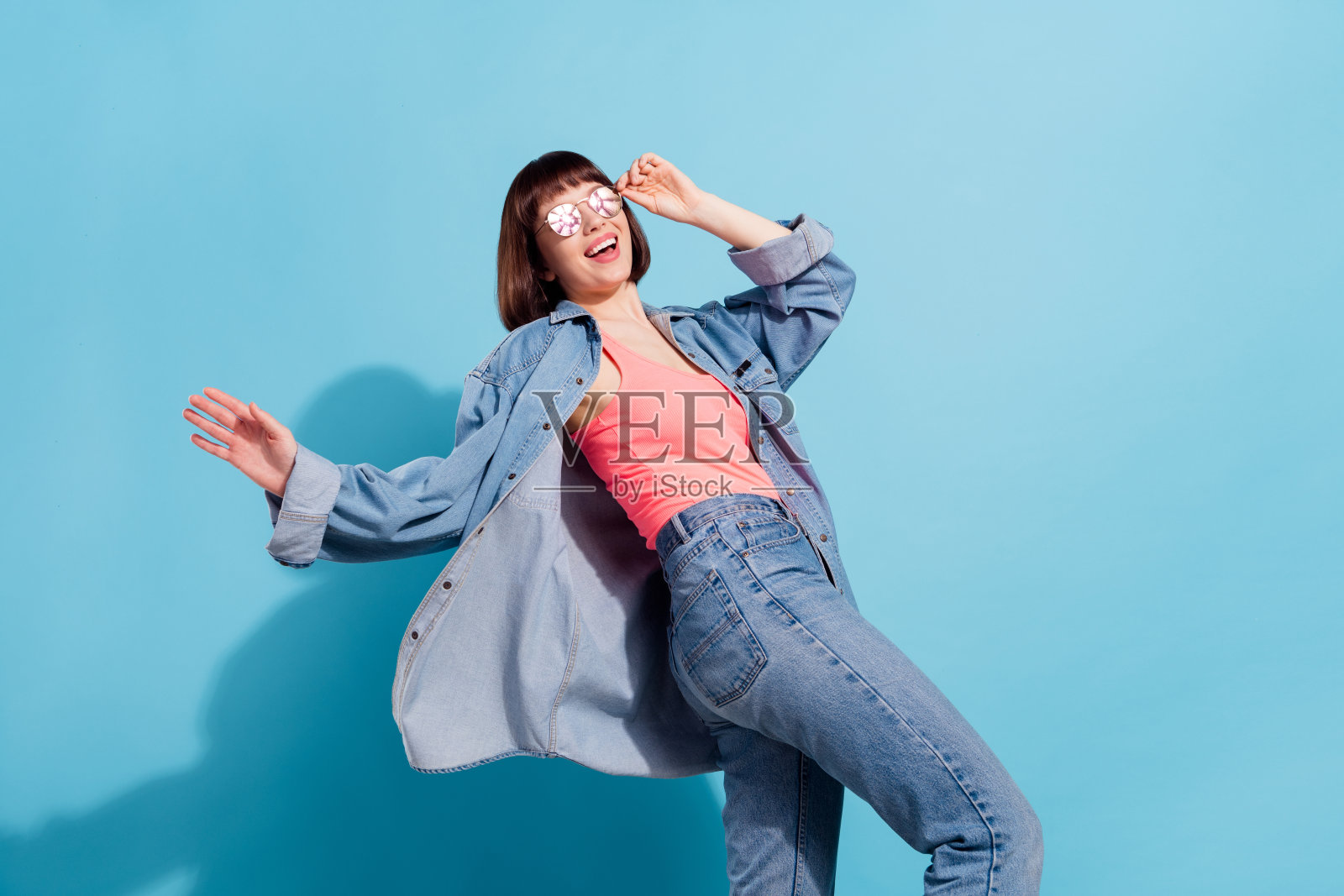 迷人、开朗的女孩肖像，在明亮的蓝色背景前快乐地跳舞、玩耍、移动并触摸眼镜照片摄影图片