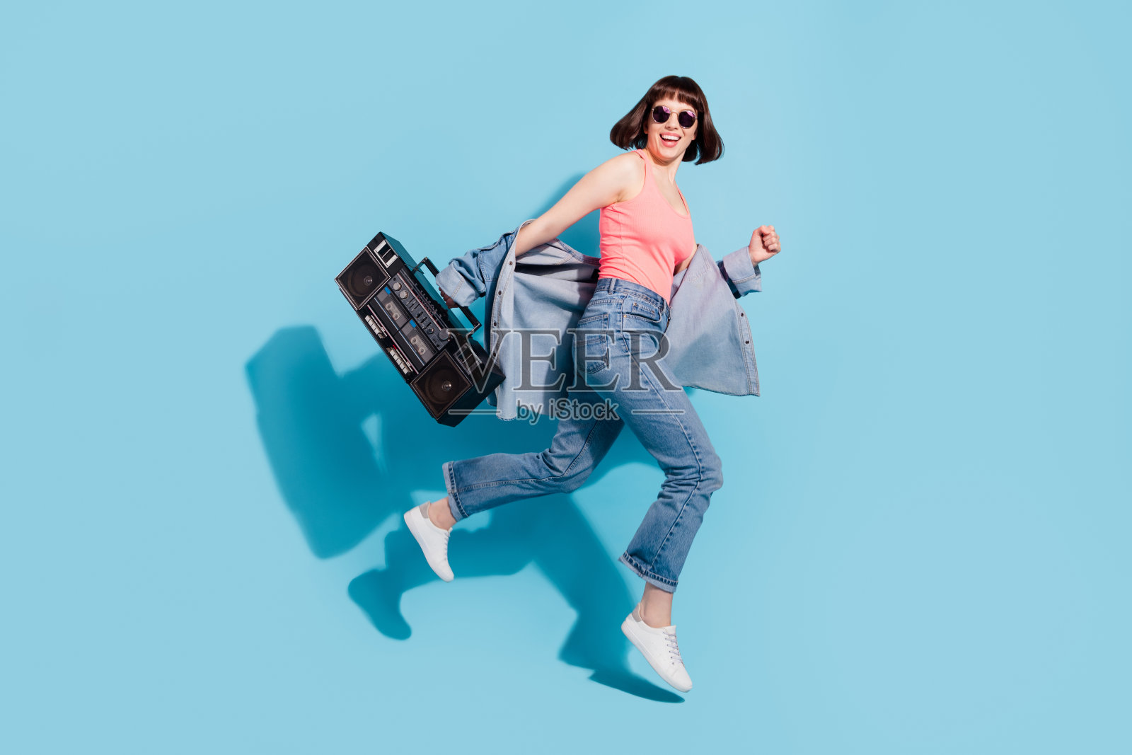 一位漂亮的、快乐的女孩，全身照，抱着一个玩家，在明亮的蓝色背景前跳跃奔跑，孤身一人。照片摄影图片