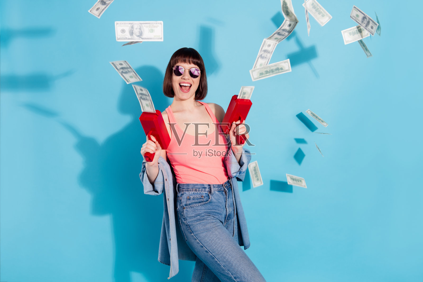 迷人的、时尚的、快乐的女孩肖像，正在玩美元，在明亮的蓝色背景下玩得很开心照片摄影图片