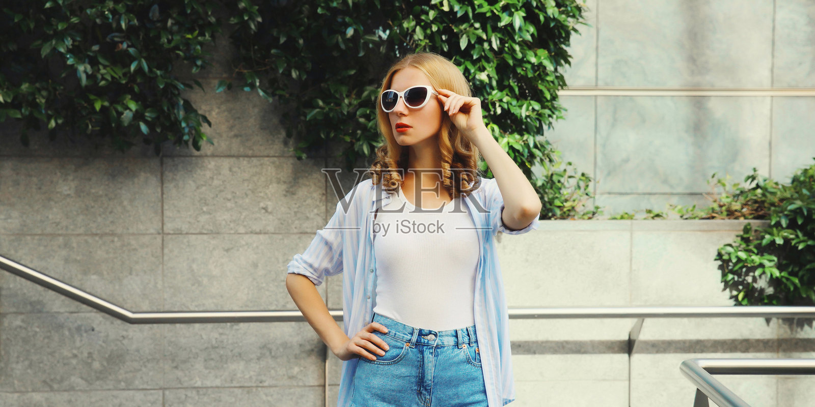 一位美丽的现代年轻女子，夏天戴着太阳镜，站在城市街道上，目光望向别处。照片摄影图片