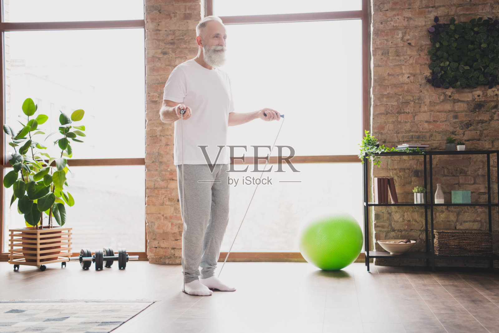 帅气微笑、积极乐观的爷爷，居家进行跳绳有氧训练的全身侧面照照片摄影图片