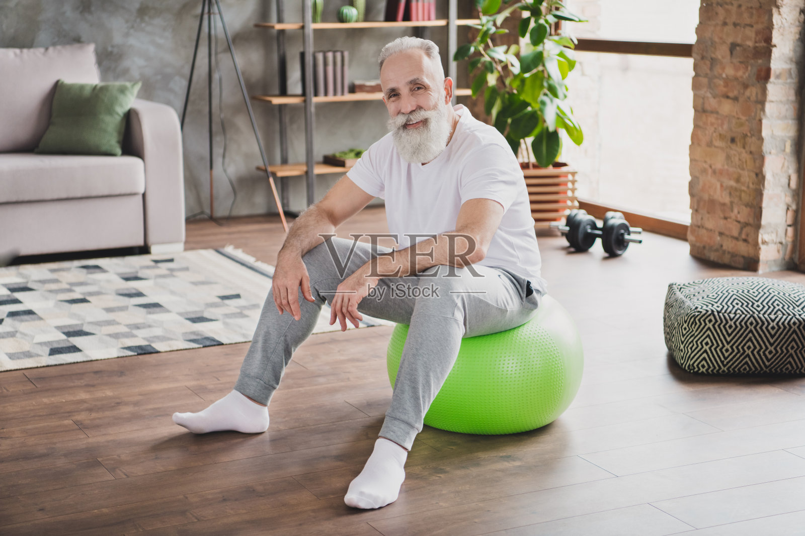 英俊、开朗、心情愉悦、面带微笑的成熟男士在家中健身球上放松的照片，尺寸为全尺寸。照片摄影图片