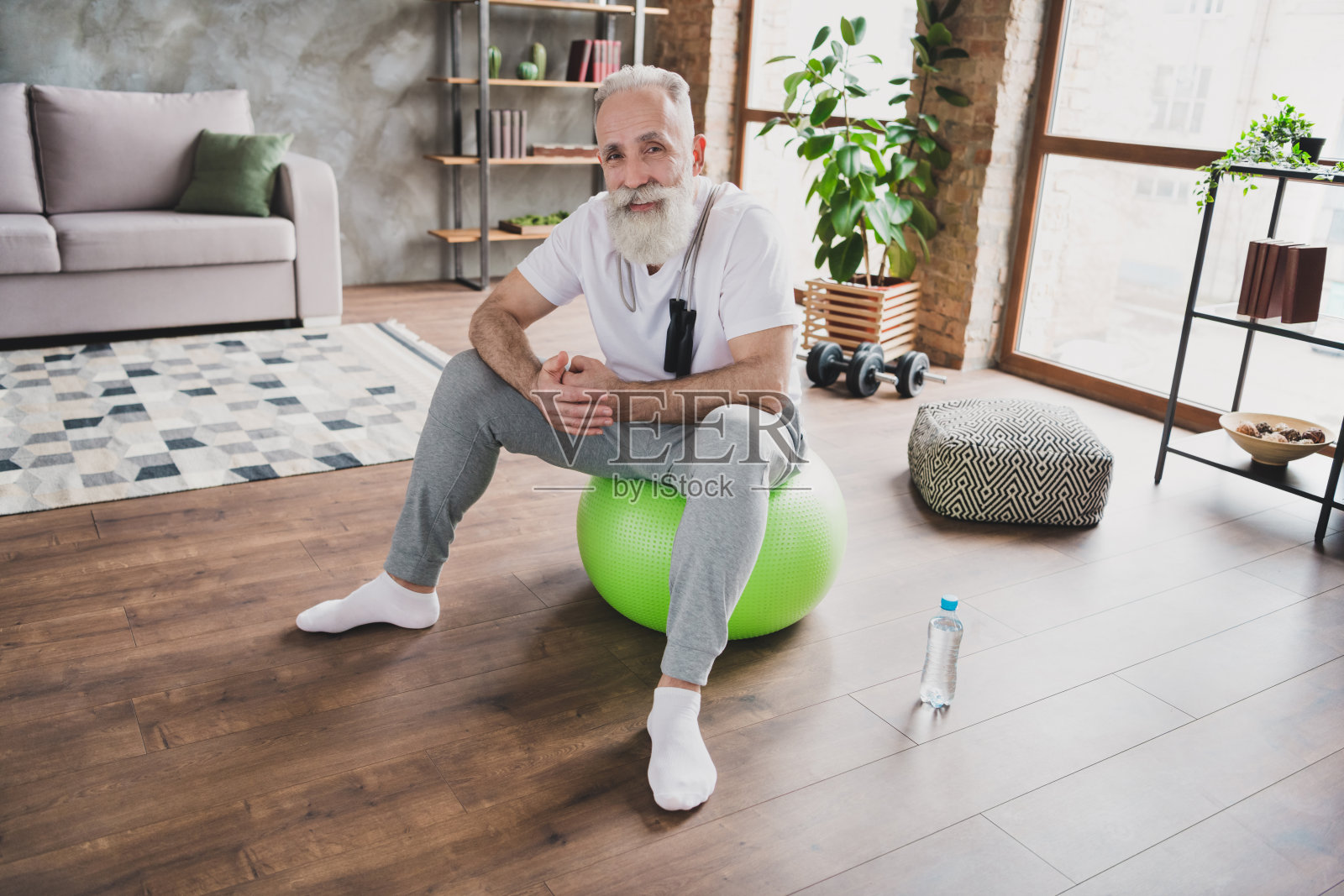 一位快乐开朗的老人坐在绿色的健身球上，心情愉悦地微笑着，在室内家庭健身房。照片摄影图片