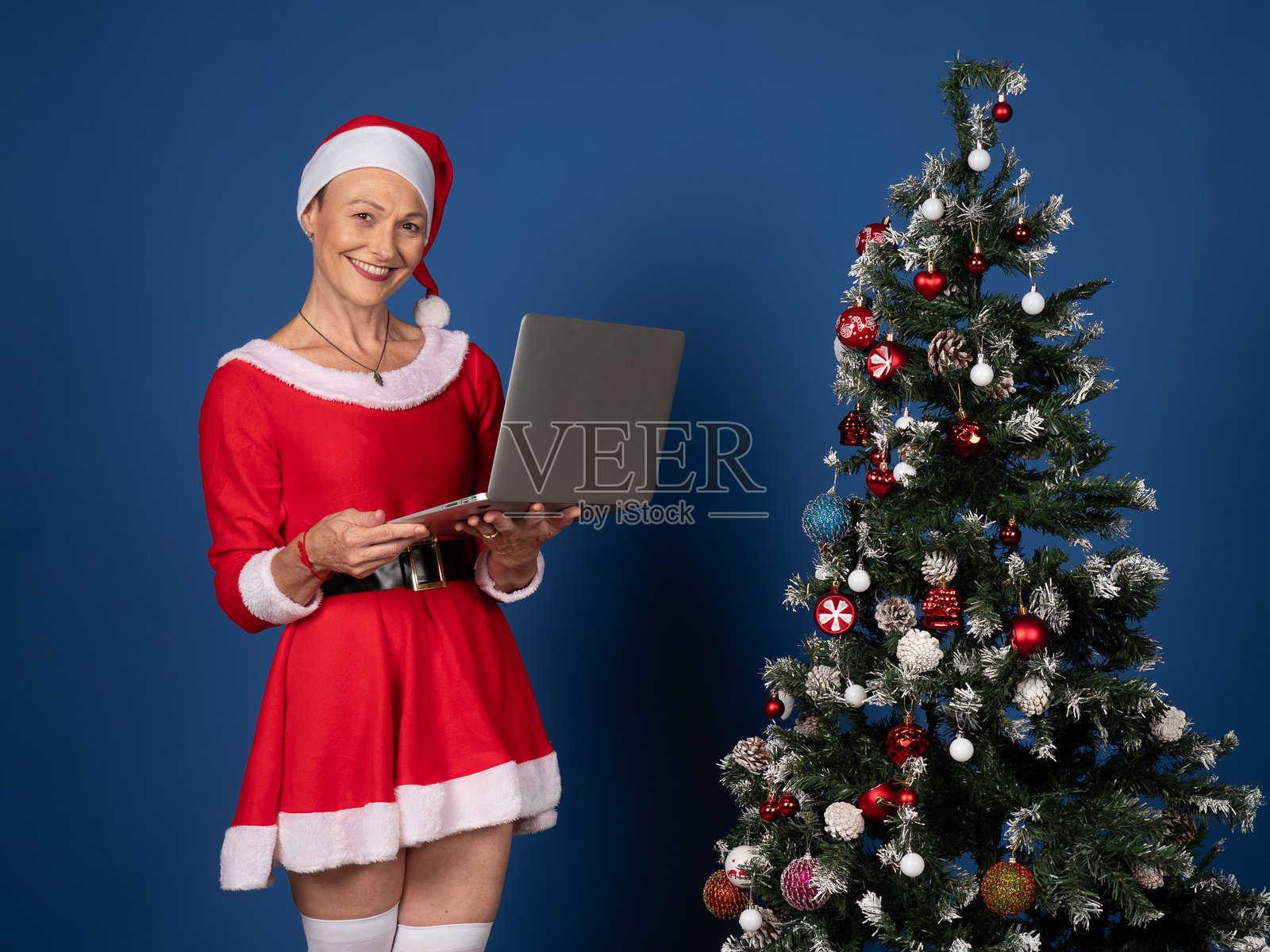 身穿圣诞老人服装的女子手持笔记本电脑进行圣诞购物照片摄影图片