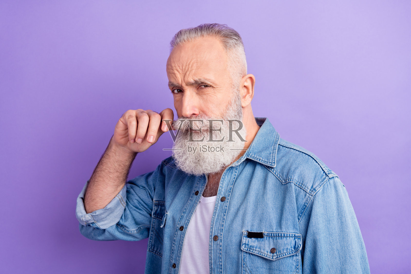 身穿牛仔服饰、蓄着小胡子、自信满满的可爱中年男子，在紫色背景前摆出造型。照片摄影图片