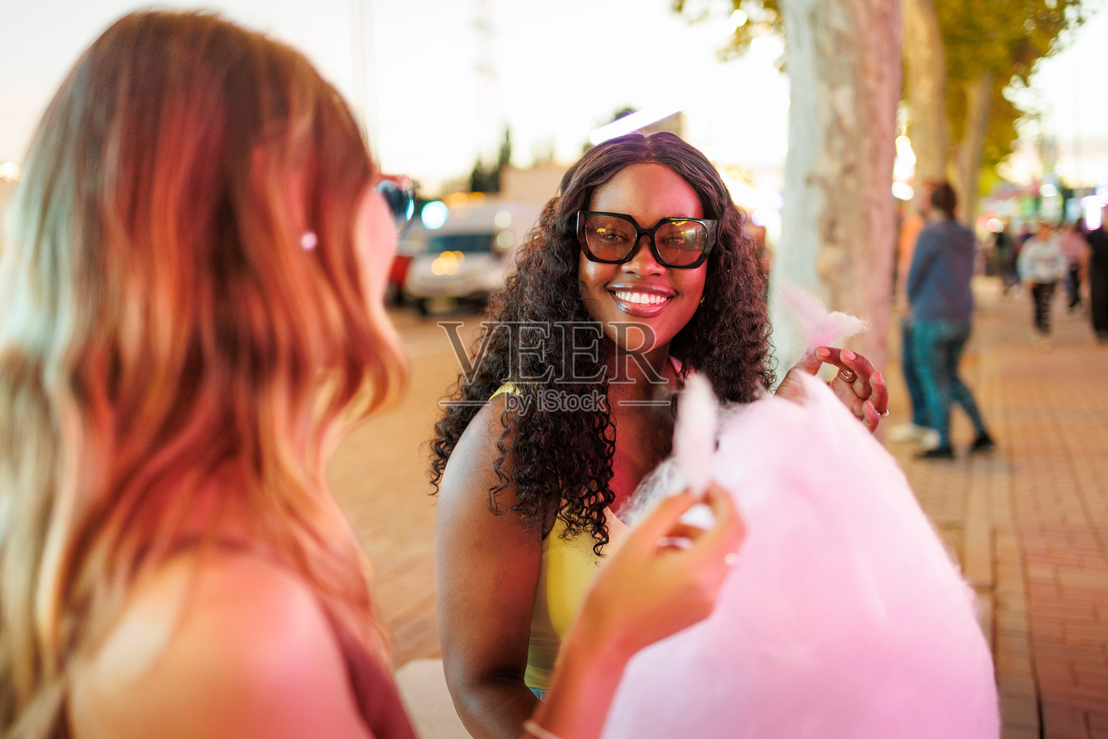 两位年轻女子在热闹的夜市上享用粉色棉花糖照片摄影图片